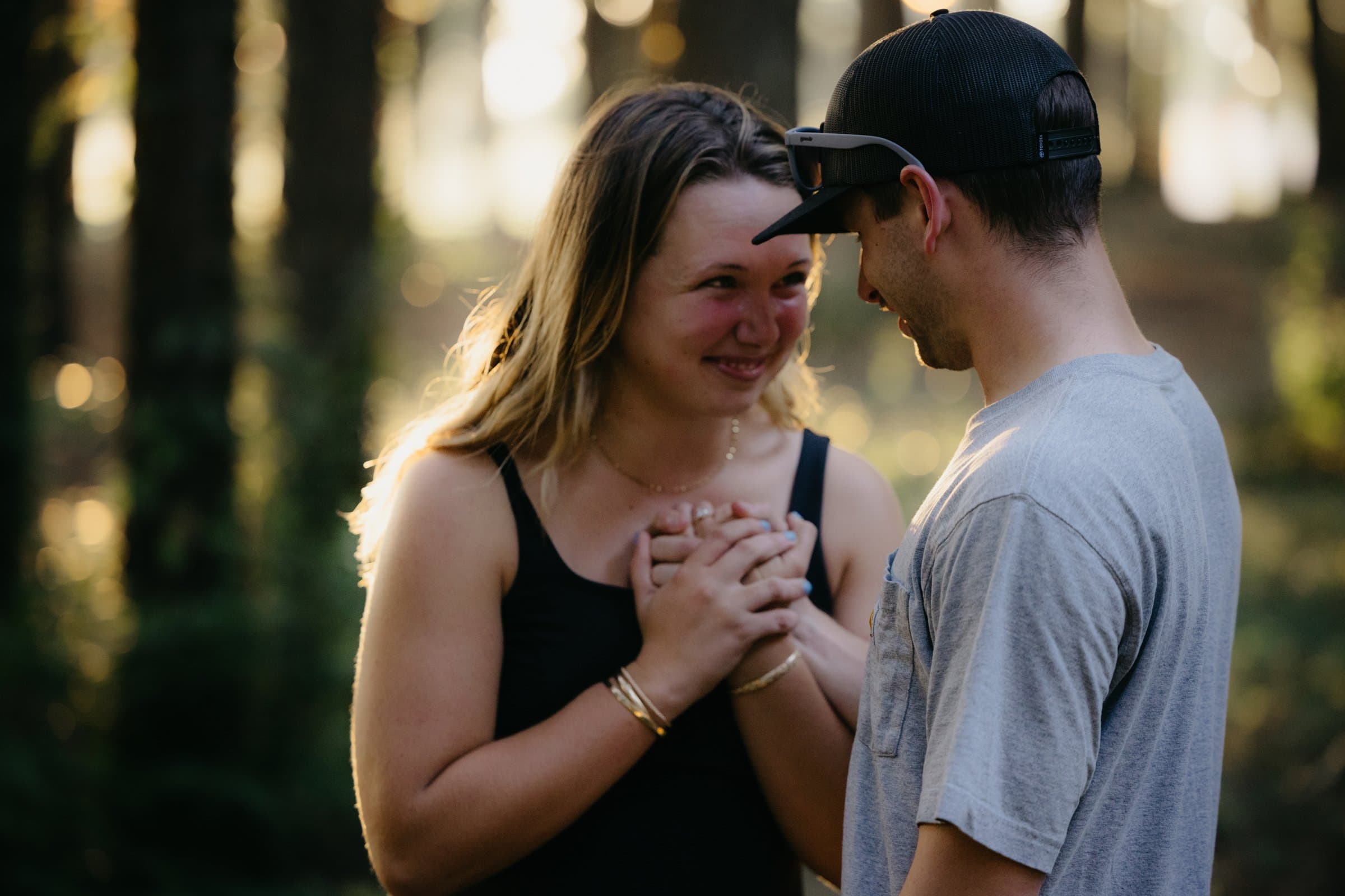 An engaged couple holding hands, her smile lit from behind