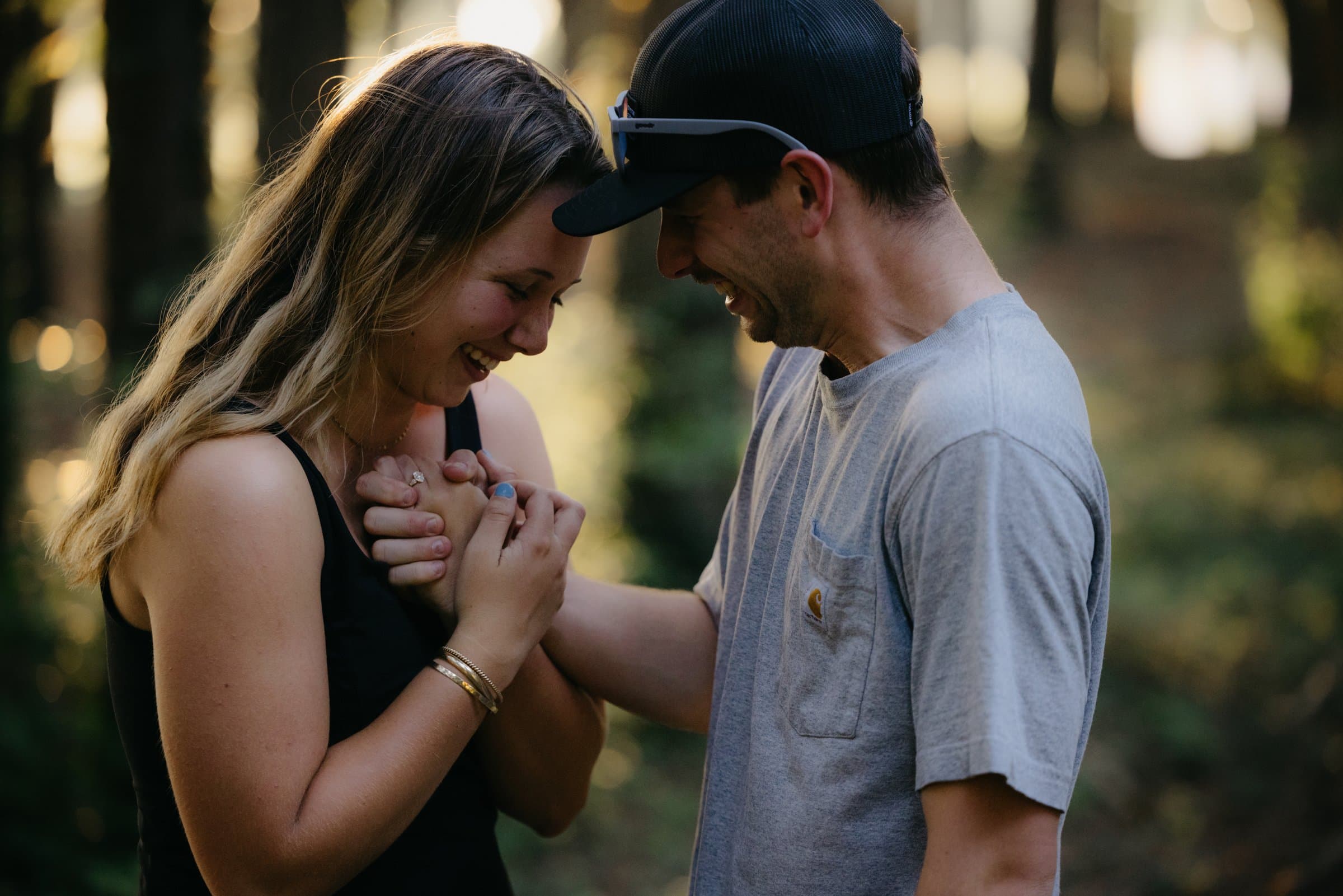 An engaged couple laughing together in the woods