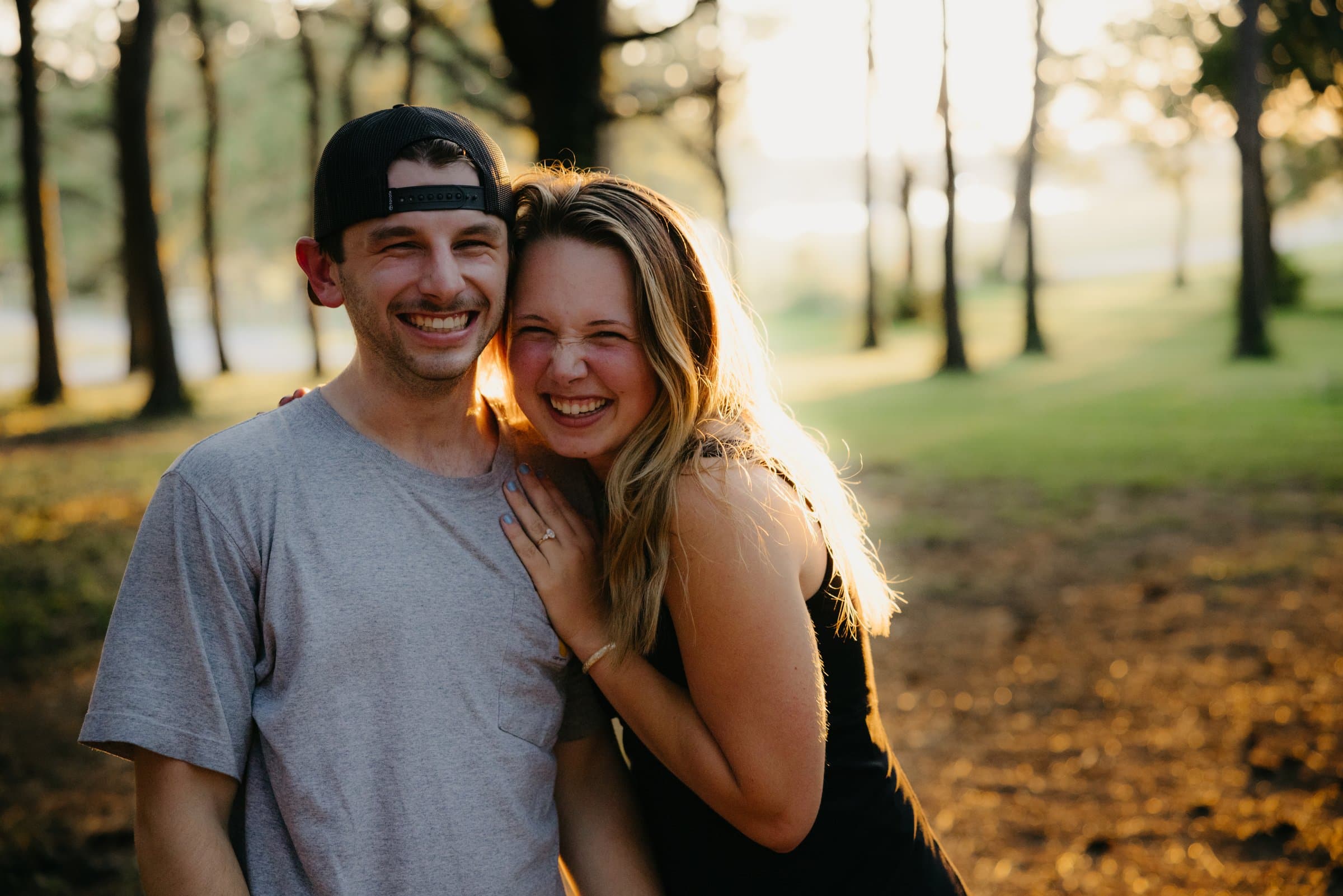 A newly engaged couple smiling at the camera at sunset