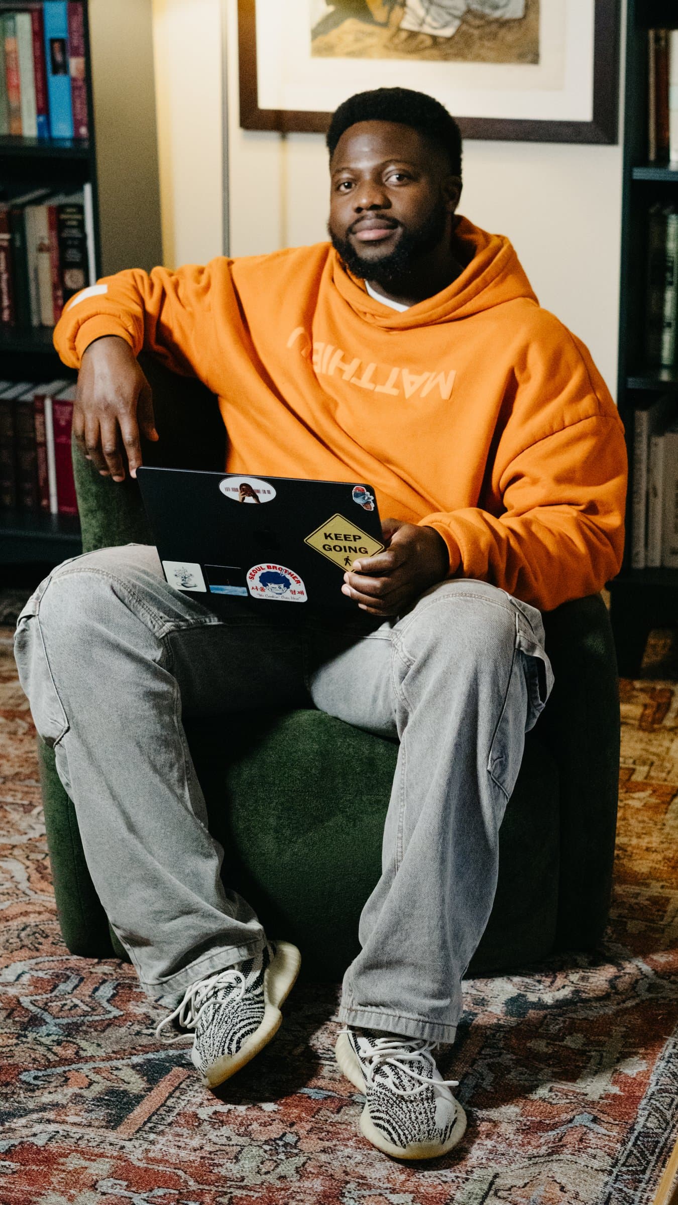 A portrait in an orange hoodie, sitting in a library chair