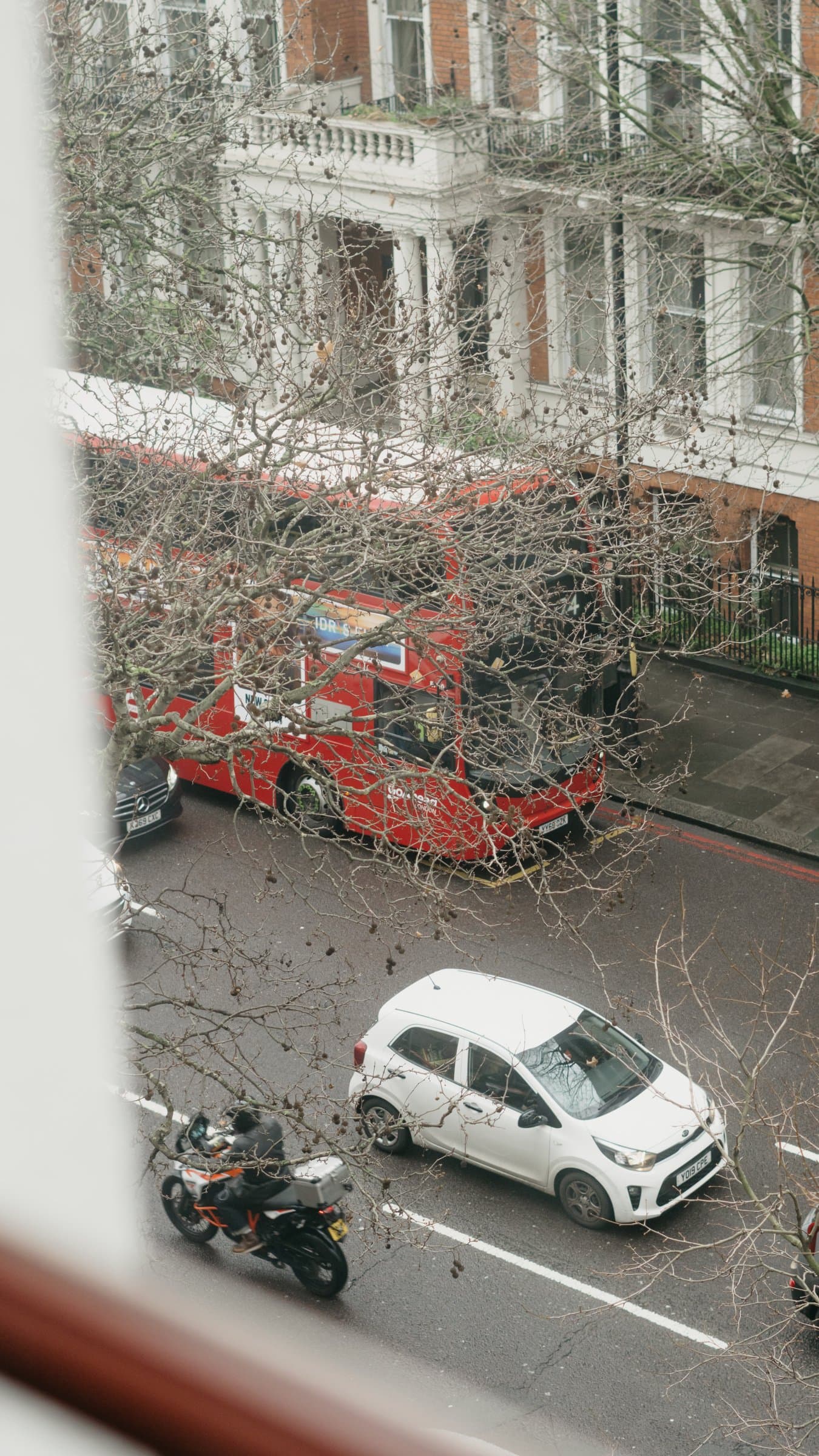 A London street with a red bus, seen through a window frame